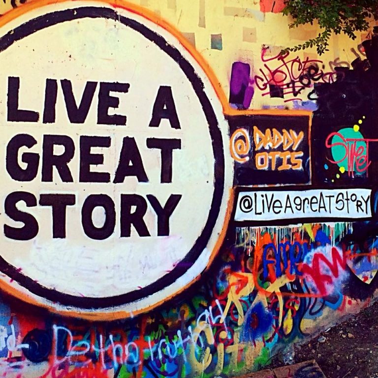 A mix of colorful graffiti on a wall, which includes a large white circle with the words “Live a Great Story” painted within it.